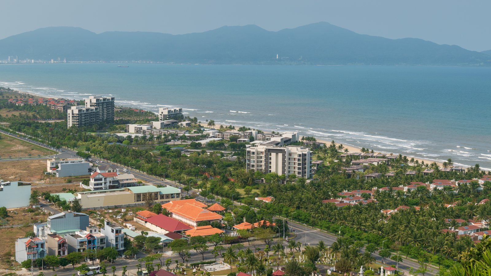 Coastal Da Nang skyline seen from above with sea, dense city blocks, and distant mountains