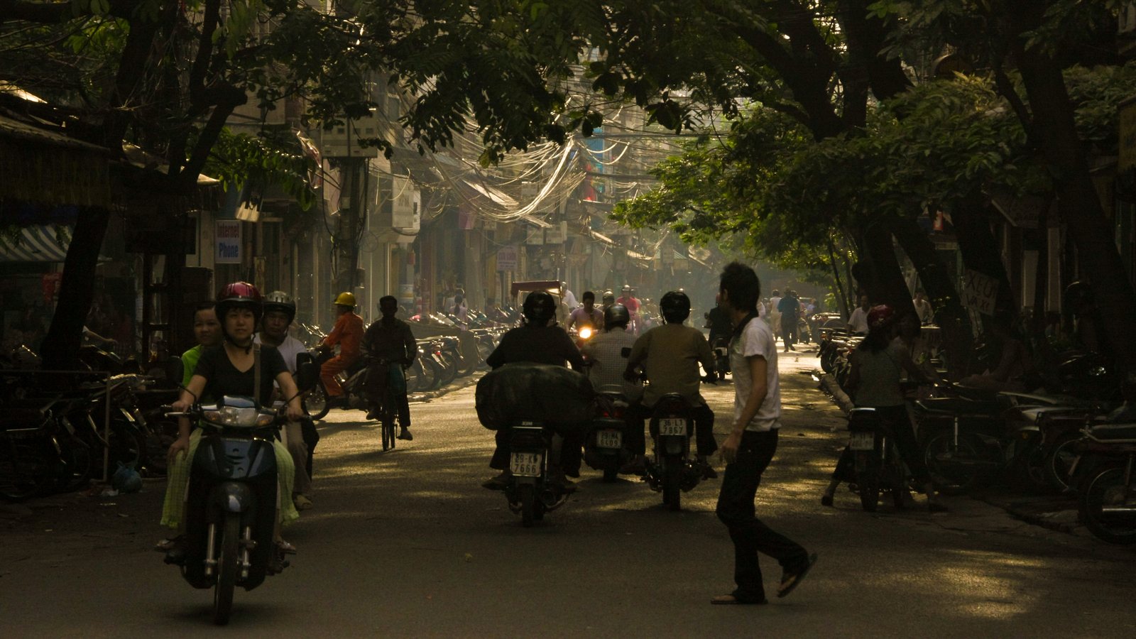 Crowded Hanoi street with dense motorbike traffic, dust, and tightly packed urban clutter