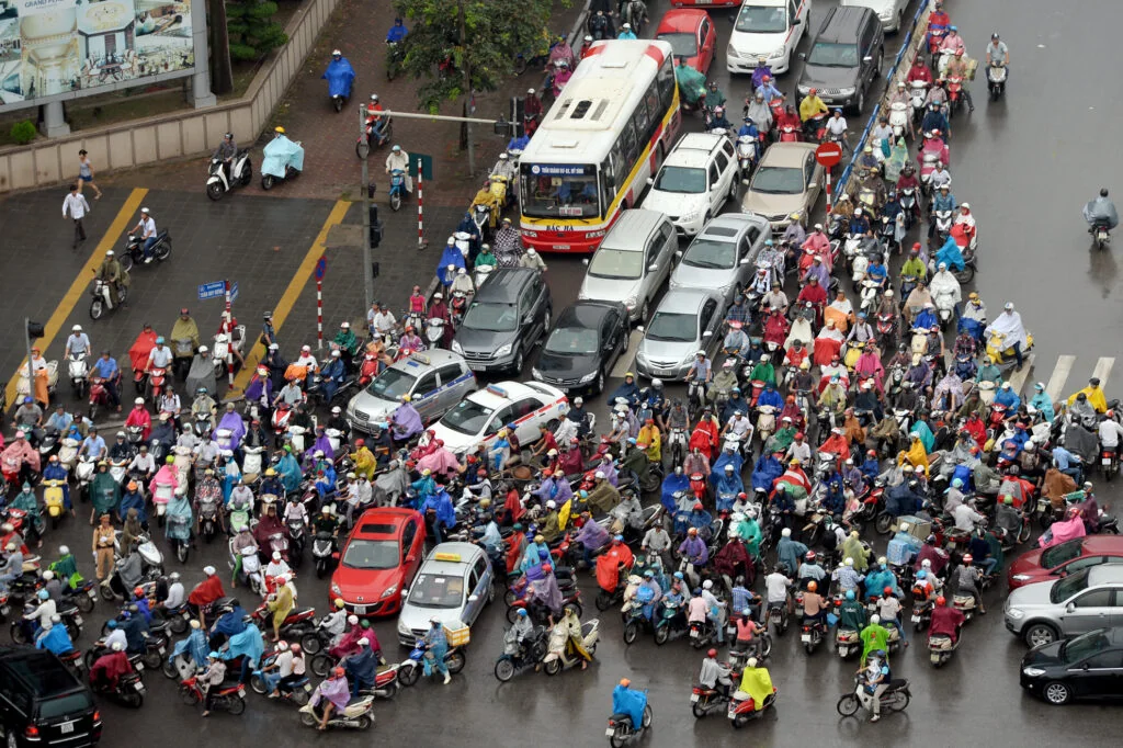 Dense Vietnamese street traffic at ground level, motorbikes clogging every angle, the kind of scene no amount of money reshapes into order